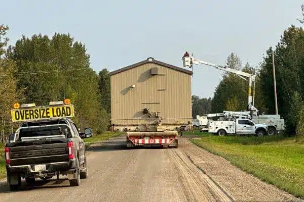 Tundra heavy hauling and rigging trucks and trailer transporting a large compressor building as Fortis Alberta lifts electrical lines to allow clearance